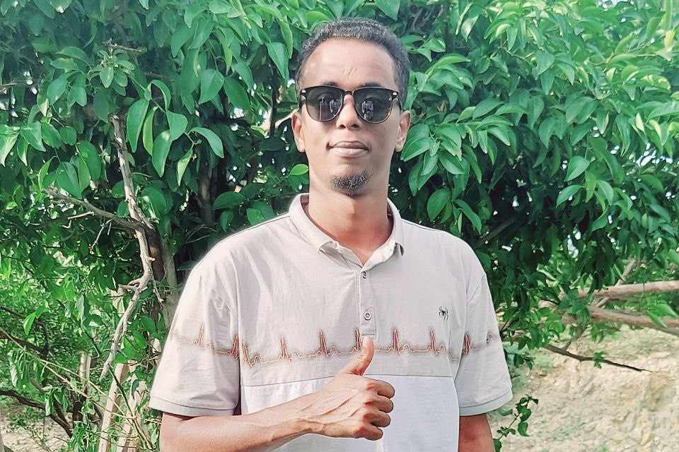 A photo of Charmake Qalinle doing a thumbs up. Posed in front of guava tree.